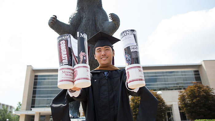 Graduating student holding posted by the bear statue.