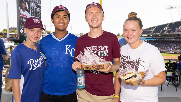 Four people take a photo together at Missouri State Day at Kauffman Stadium 