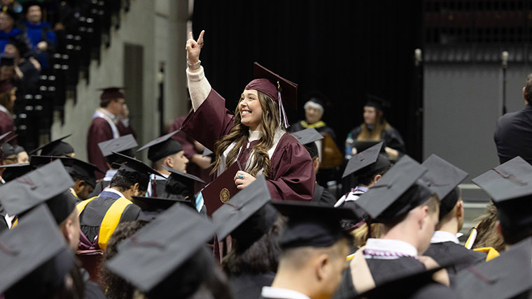 An excited Missouri State student smiling and waving during her commencement ceremony.