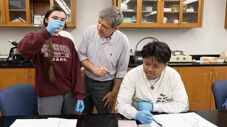 Two students and a professor looking at samples in a biology lab class.