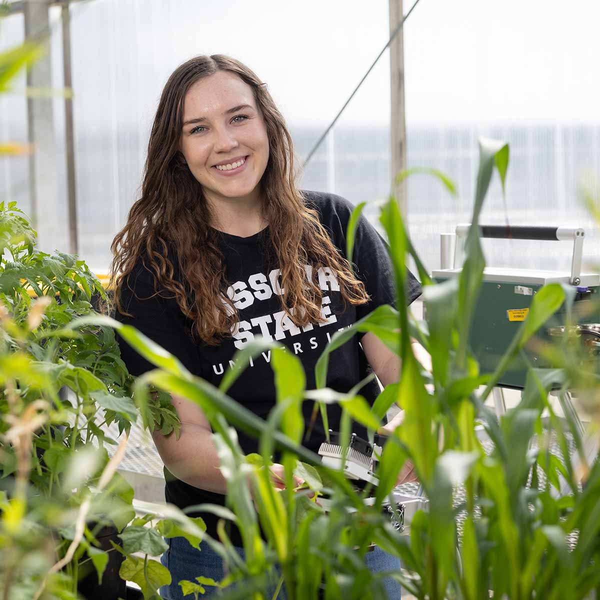 Biology graduate student Lyndsey Rightnowar smiles while tending to plants in a greenhouse.