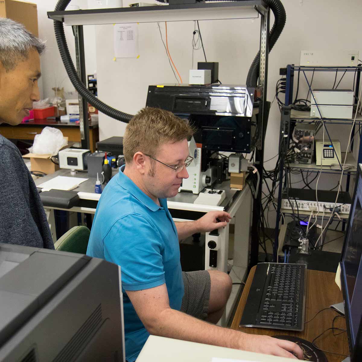 A biology student conducts research on a computer in a lab while Dr. Kyoungtae Kim observes.