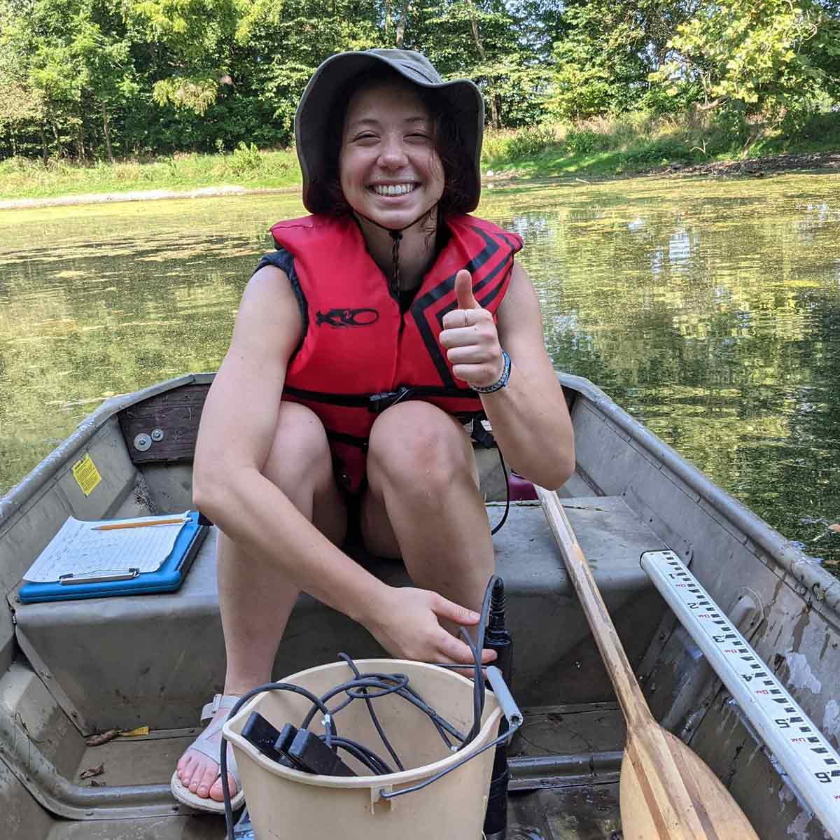 Daphne Miles smiling and giving a thumbs up on a boat while conducting aqautic plant research