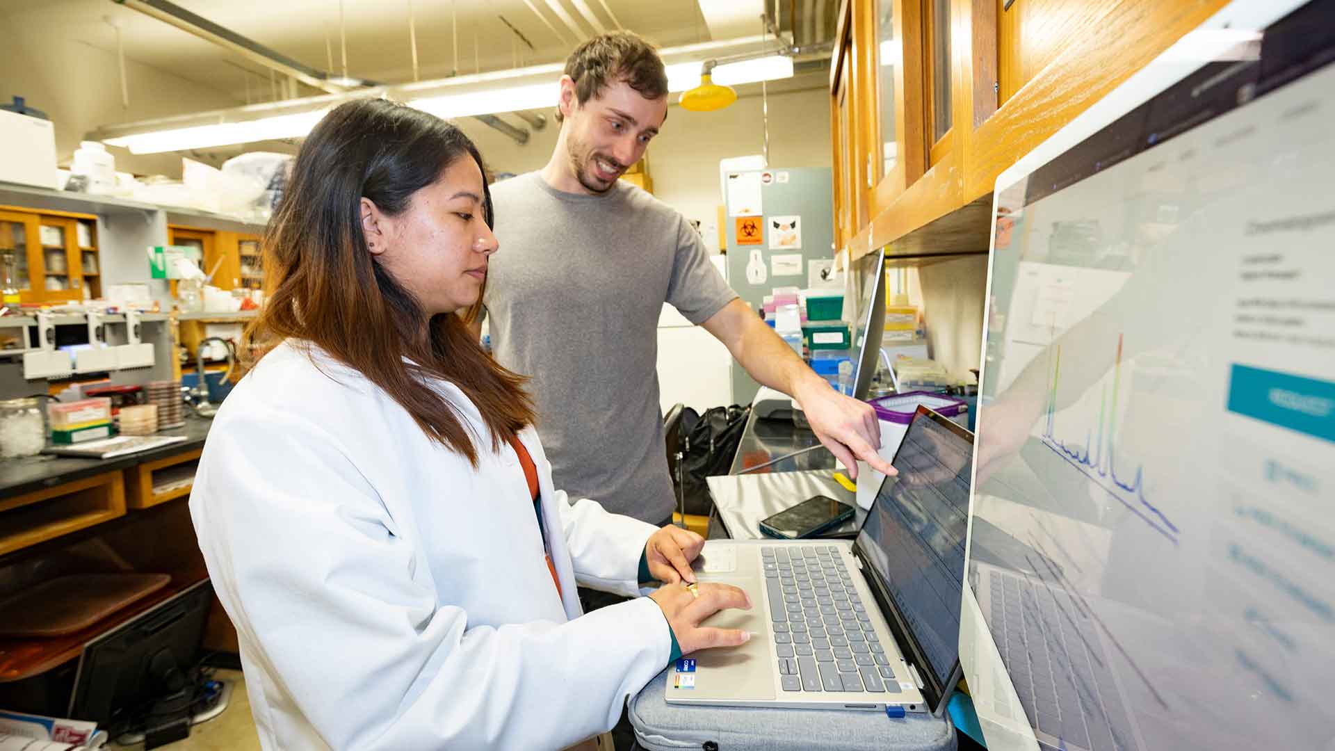 Two biology graduate students look at data on a computer monitor in a lab.