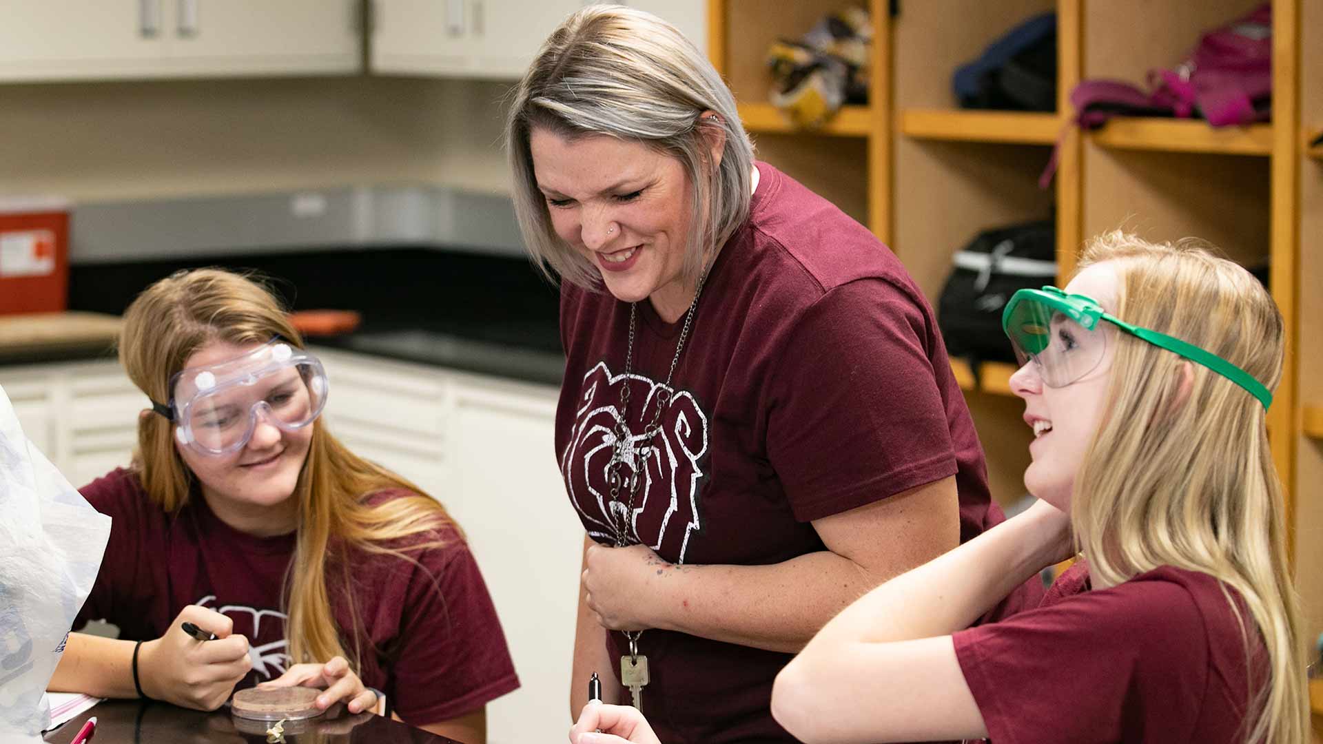 A science teacher sharing a laugh with two students during a lab class.