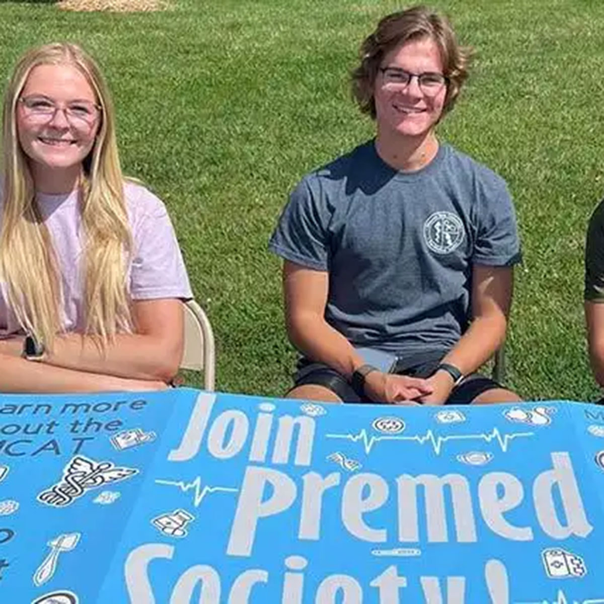 Three students sitting at a table for the pre-medical society during a campus event