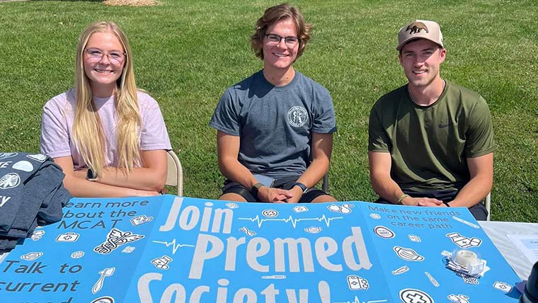 Three students sitting at a table for the pre-medical society during a campus event.