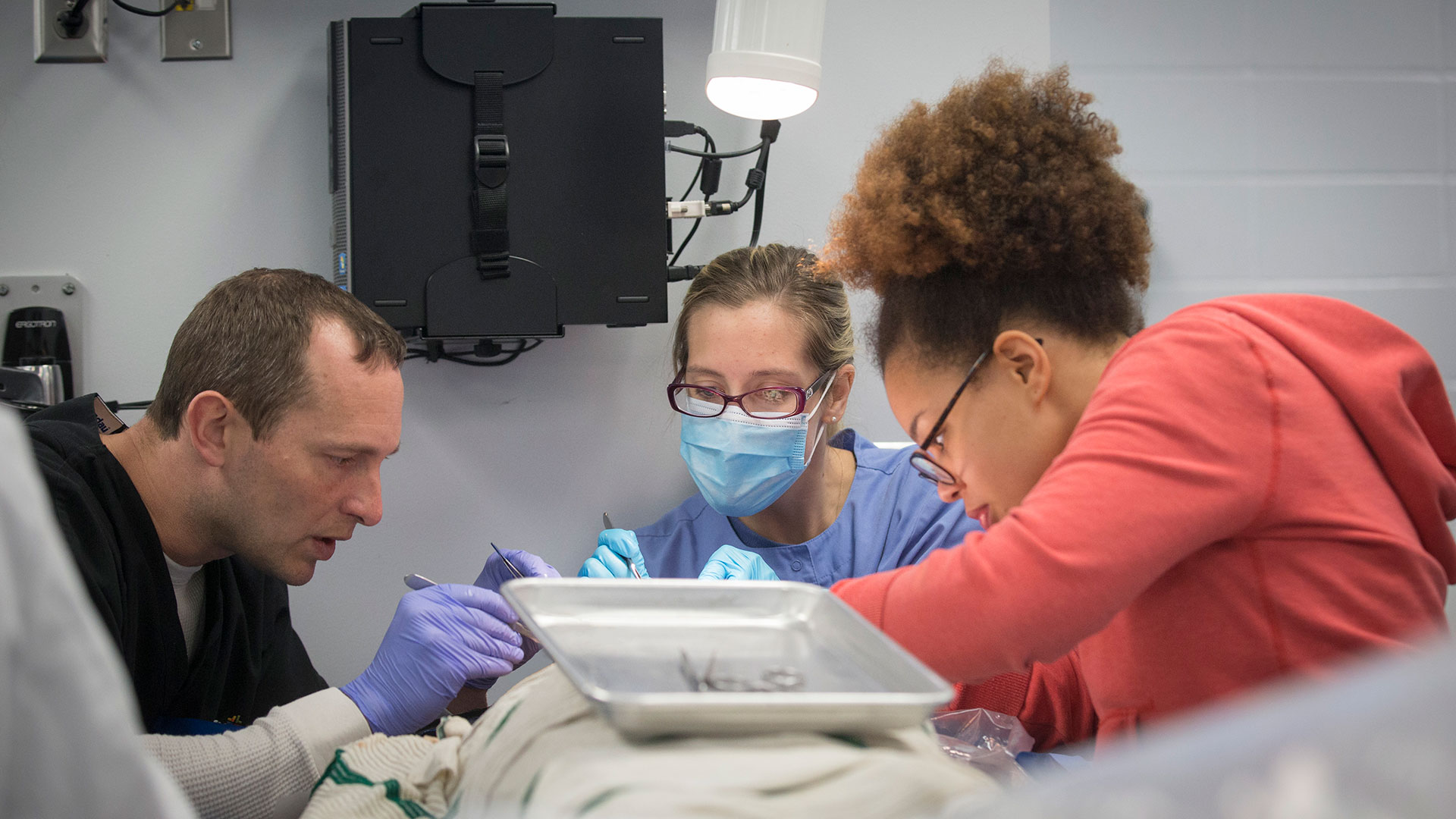 Three students use medical tools on a practice body during their anatomy class.