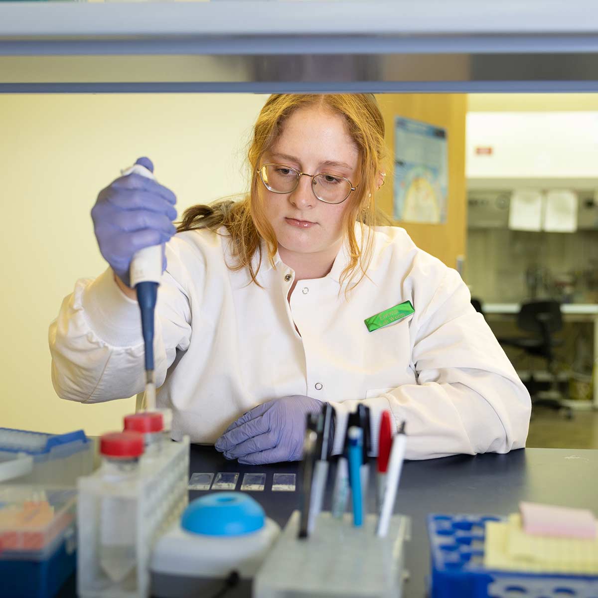 A biology student in a white lab coat conducts research work inside Jordan Valley Innovation Center