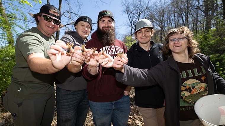 Five biology students hold up crawfish they caught on a field trip to a local stream.