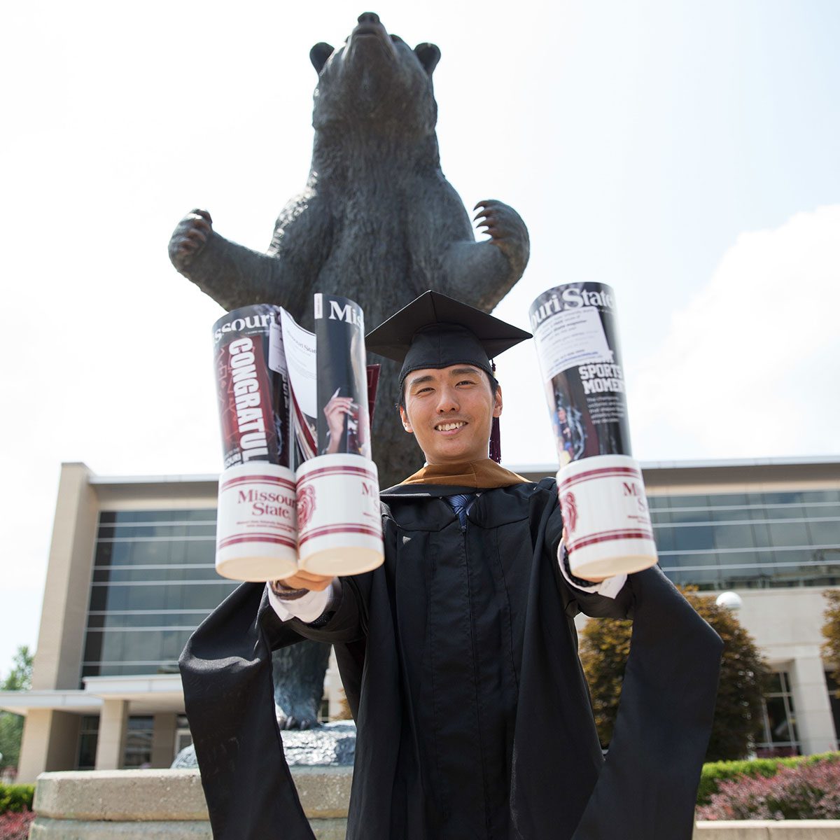 An MSU graduate holds Missouri State promotional materials in front of a Bear statue.